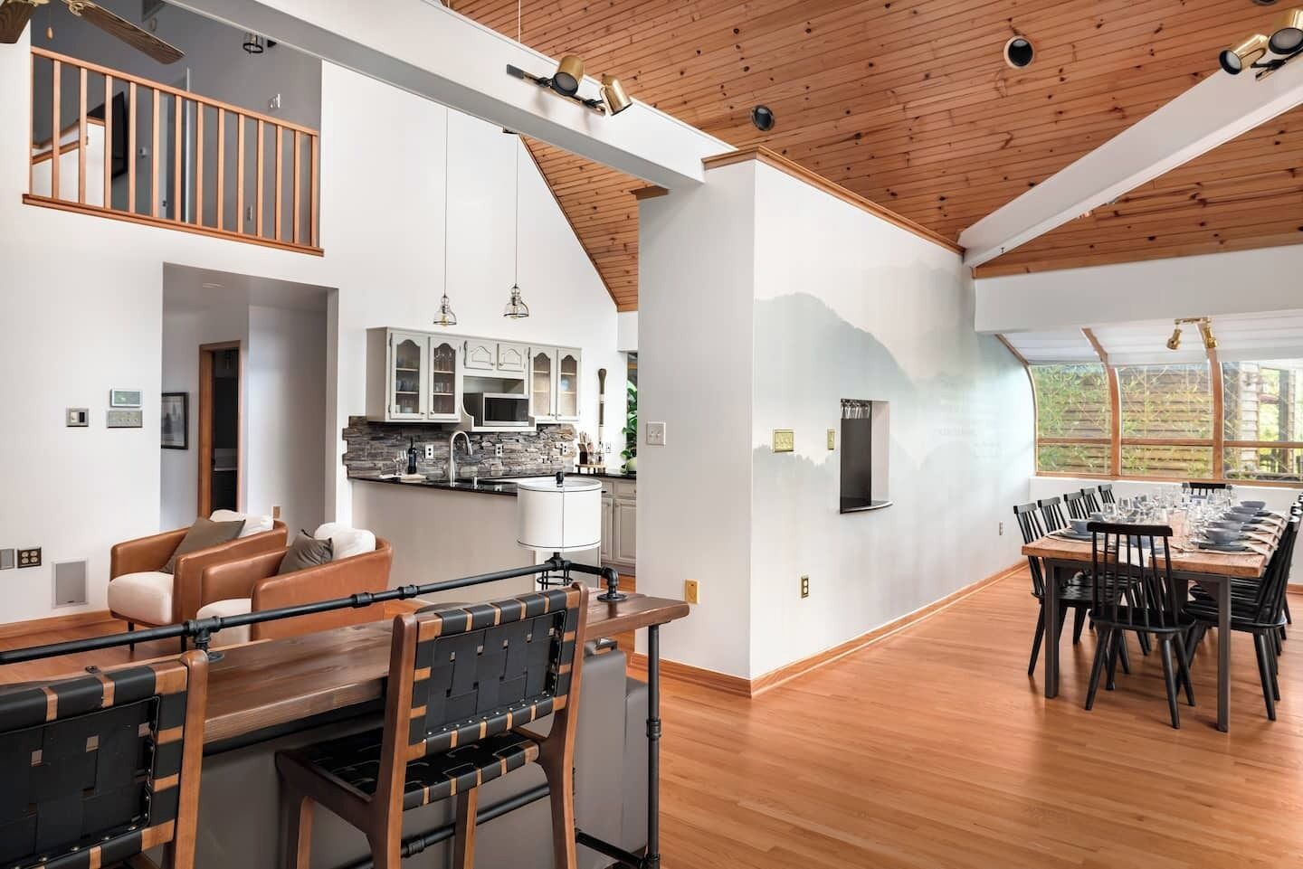 A spacious living area with a dining table and chairs, a kitchen with modern appliances, and a high ceiling with wooden beams.