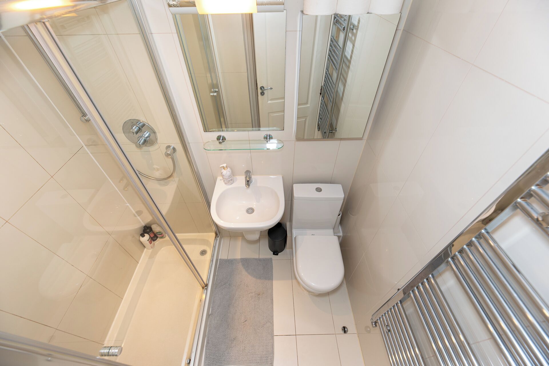 Un baño pequeño con cabina de ducha de vidrio, lavabo pedestal y retrete.