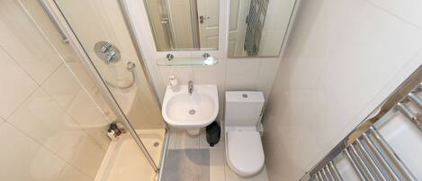 Un baño pequeño con cabina de ducha de vidrio, lavabo pedestal y retrete.