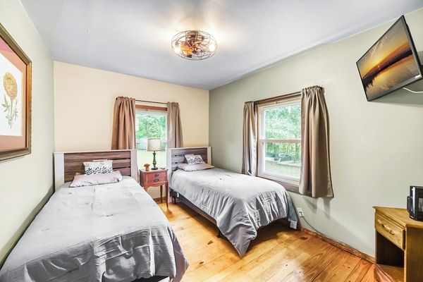 Bright bedroom with two twin beds, large windows, and a wall-mounted TV, offering a peaceful view of the outdoors.
