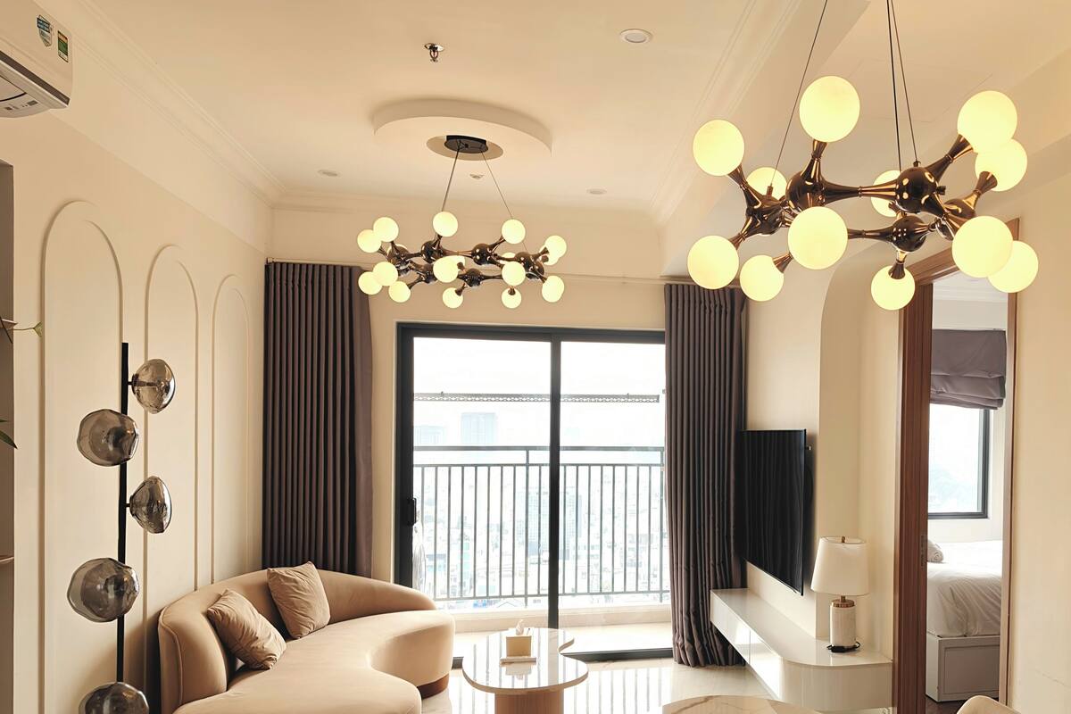 A modern living room with a curved sofa, a marble coffee table, and a chandelier with multiple spherical lights.