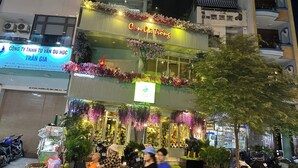 A building with a sign reading "Con Qia Trang" and a neon sign above. There are motorcycles parked in front, and a person is riding a scooter. - Soho Residence-Tony Apartment (Ho Chi Minh City)