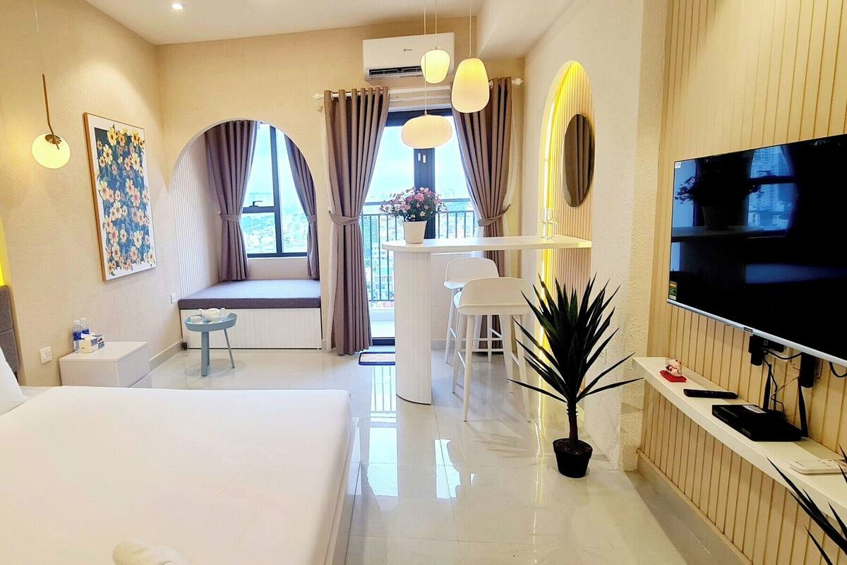 A modern hotel room with a large bed, a desk, a TV, and a balcony with a view.