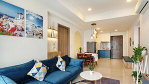 A modern living room with a blue sofa, a round coffee table, and a dining area with a table and chairs. - Soho Residence-Tony Apartment (Ho Chi Minh City)
