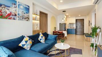 Ein modernes Wohnzimmer mit einem blauen Sofa, einem runden Couchtisch und einem Essbereich mit Tisch und Stühlen.