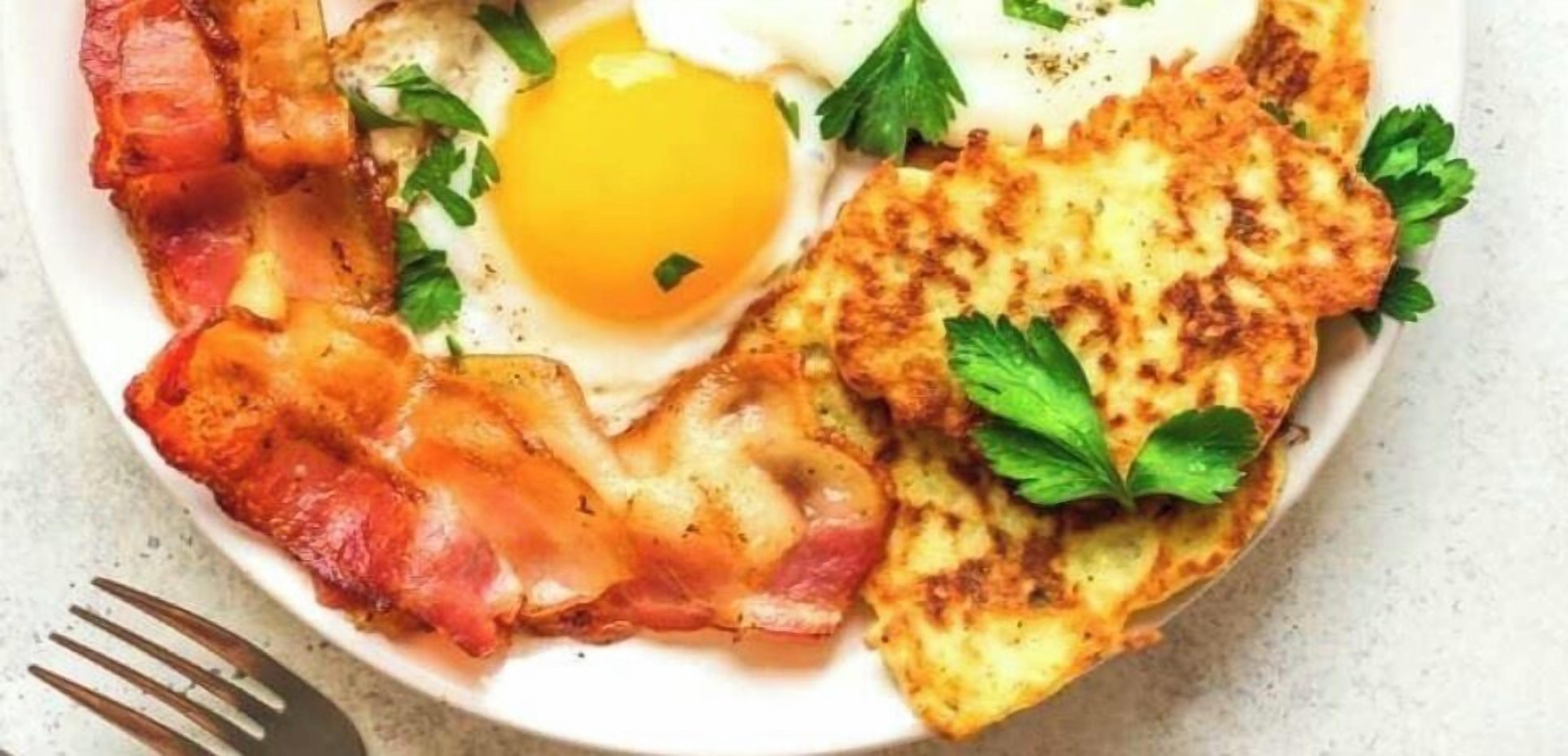 Un plato con tocino, huevos y patatas ralladas.