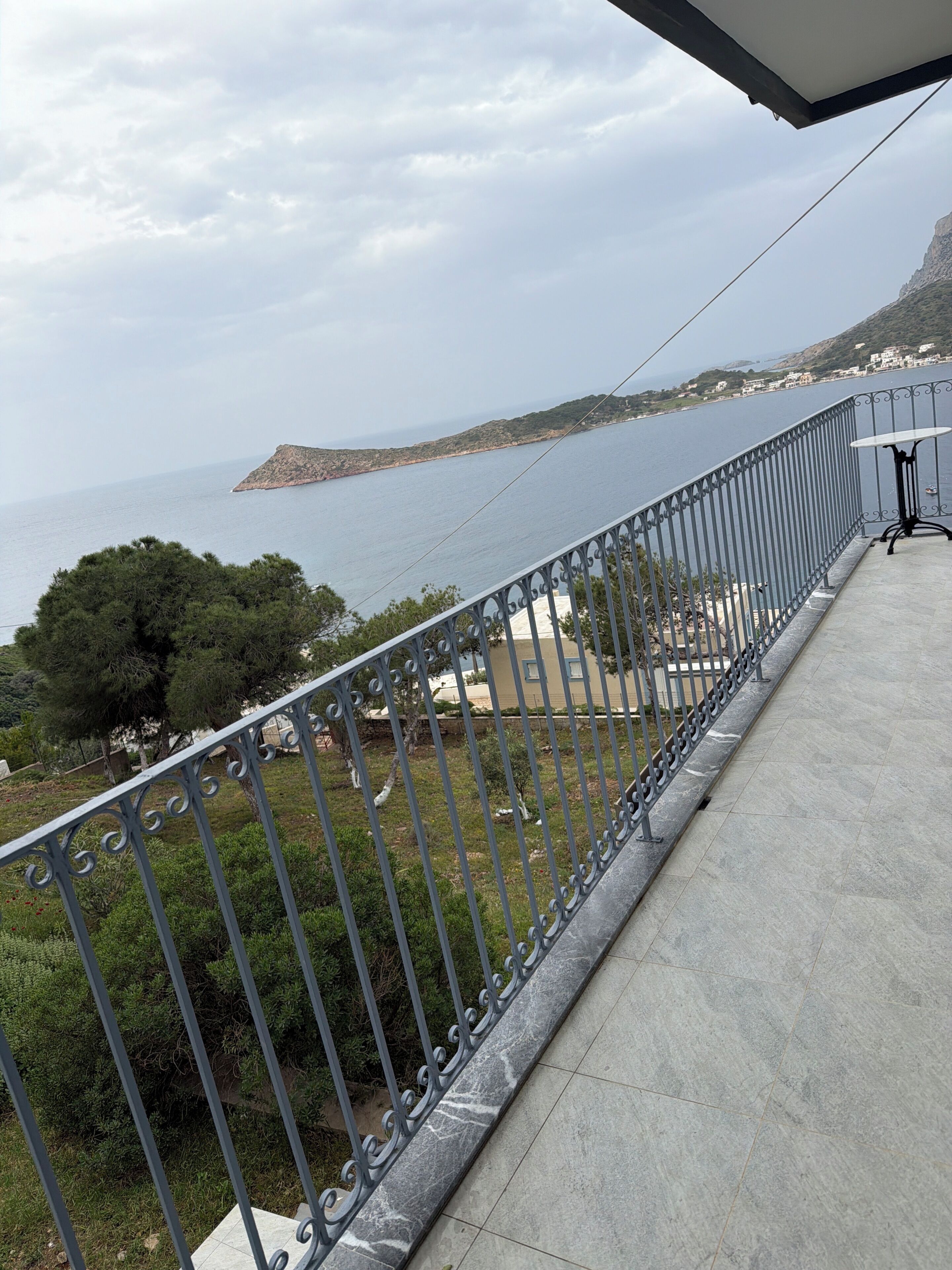 En balkon med gelænder i metal, der giver udsigt over et kystlandskab med vand og land i det fjerne.