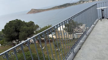 En balkon med gelænder i metal, der giver udsigt over et kystlandskab med vand og land i det fjerne.