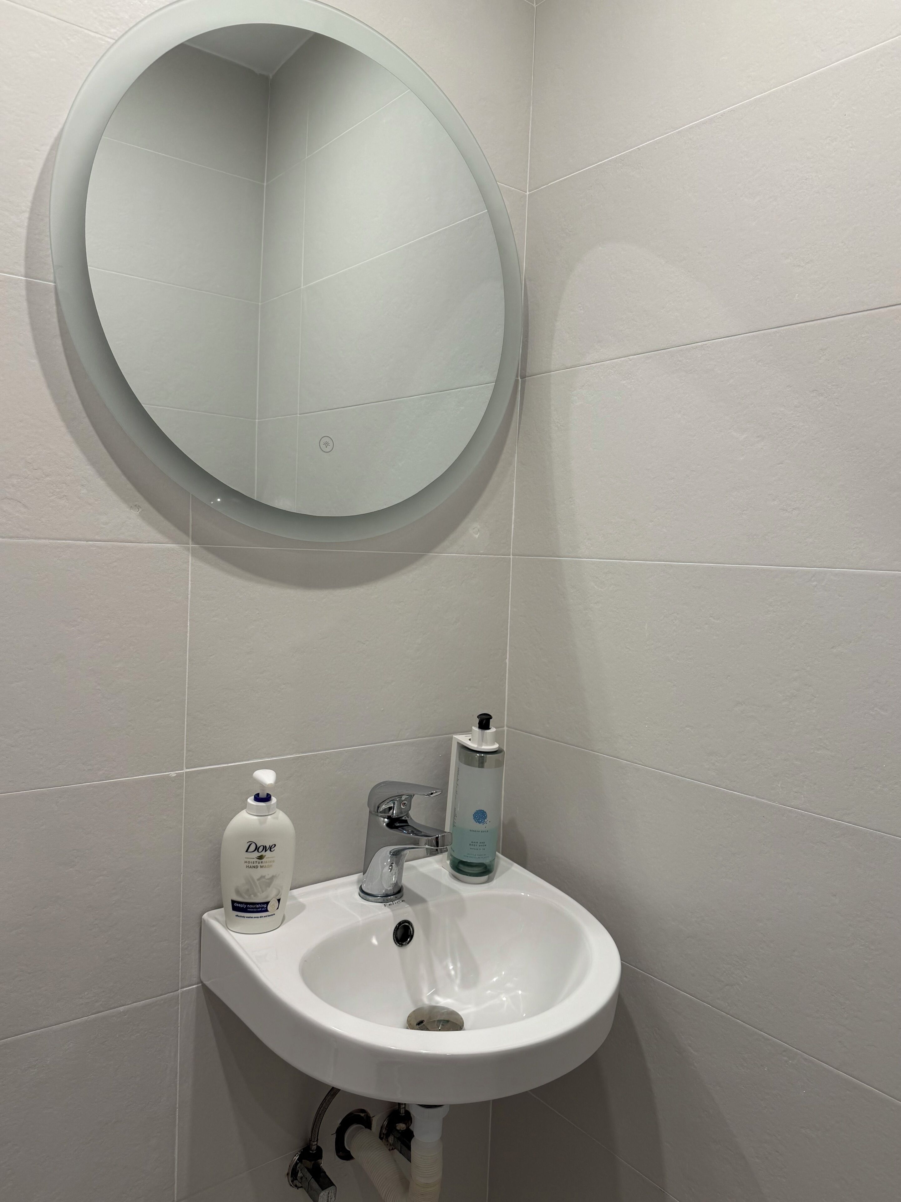 A bathroom with a white sink, a round mirror, and a hand sanitizer dispenser.