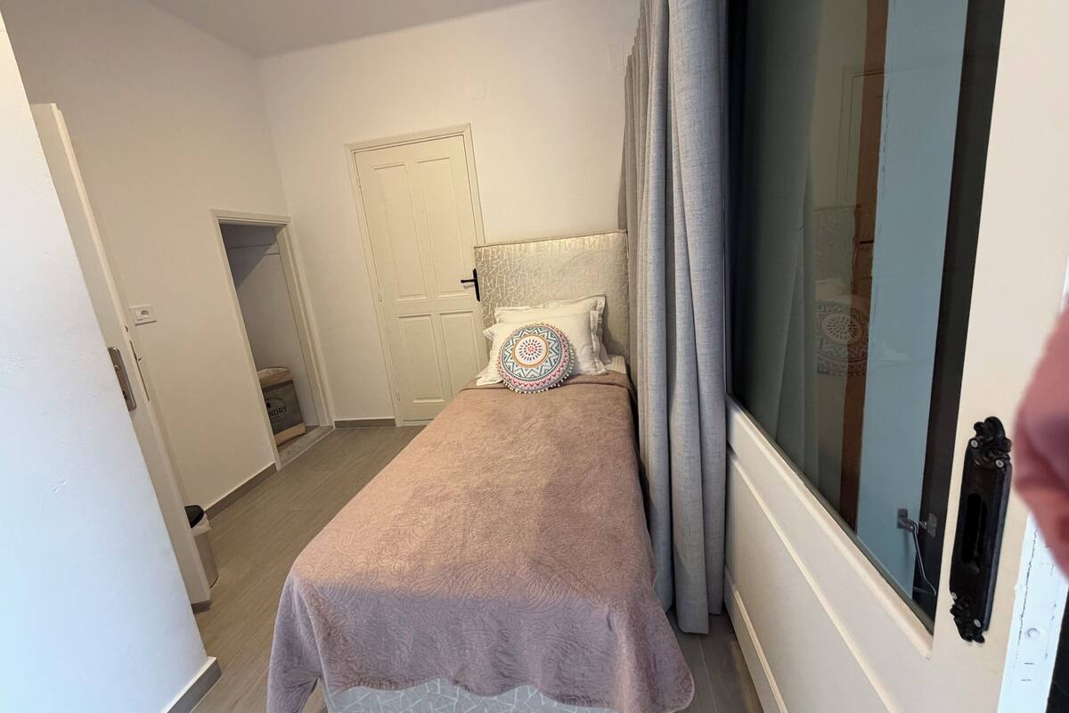 Une chambre à coucher avec un lit, une porte, une fenêtre avec des rideaux et une petite statue accrochée au mur.