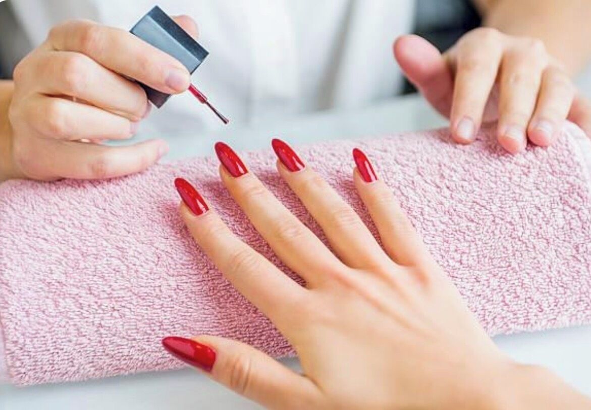 Una mano con esmalte rojo siendo secada sobre una toalla rosa.