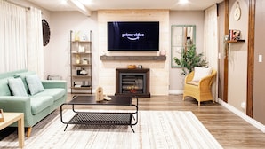 A living room with a fireplace, a television displaying 'prime video', a sofa, a coffee table, and a bookshelf. - Charming Retreat: King Bed, Full Kitchen & Spacious Backyard. Perfect Location! (Hillsboro)