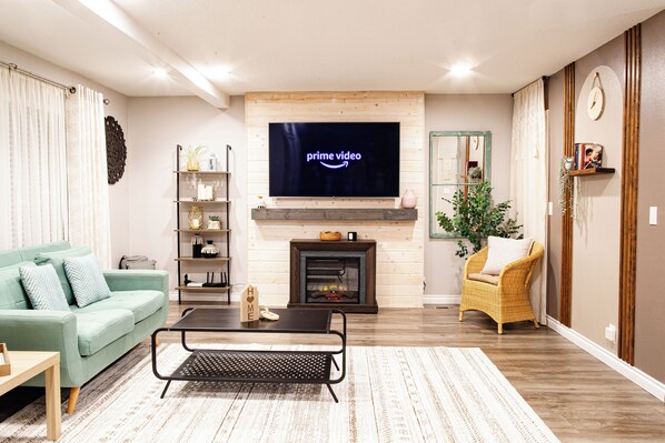 Een woonkamer met een open haard, een televisiescherm waarop 'Prime Video' wordt weergegeven, een bank, een salontafel en een boekenkast.