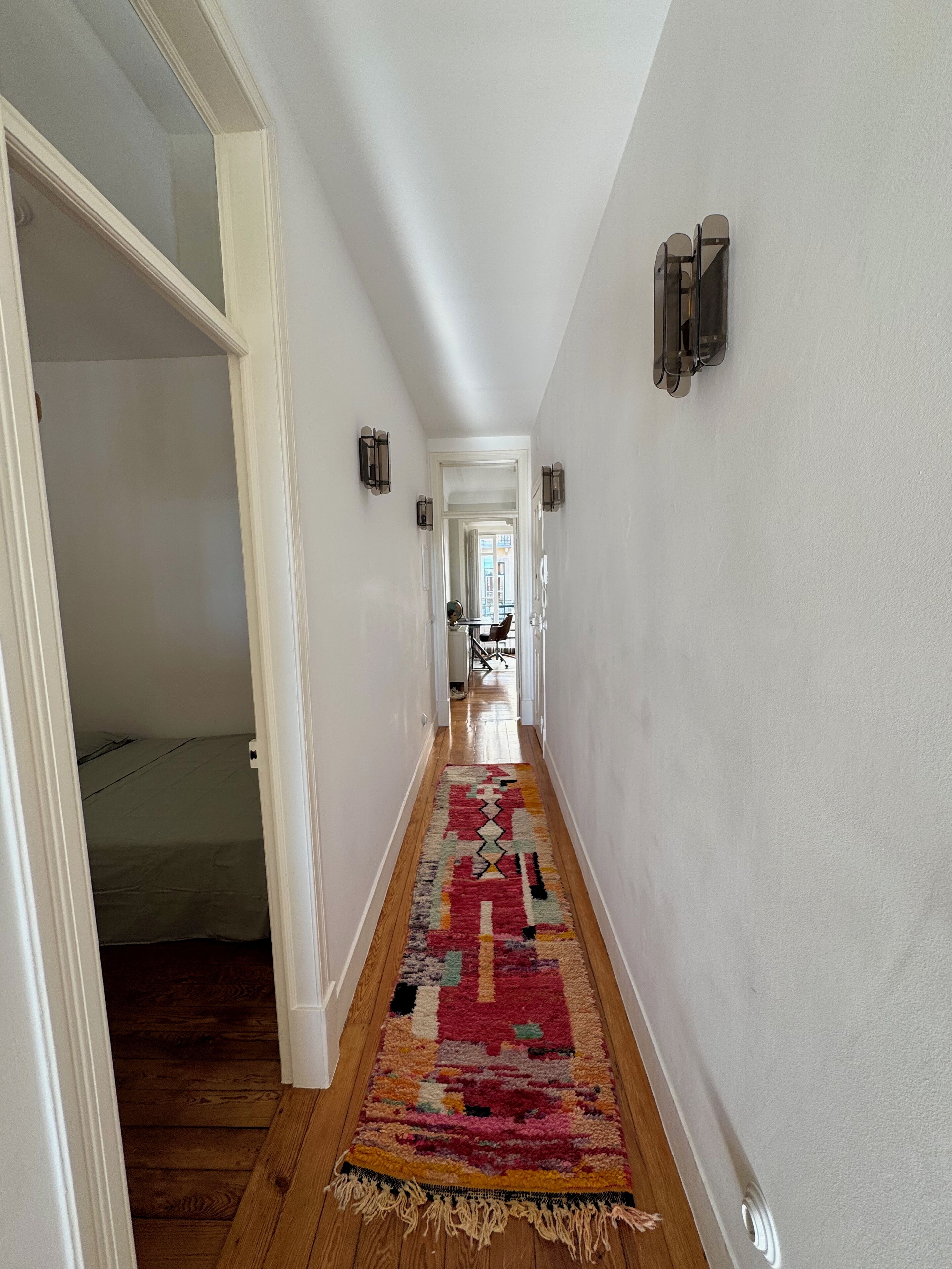 Ein Korridor mit Teppichmuster, weißen Wänden und einer Tür zu einem Zimmer.