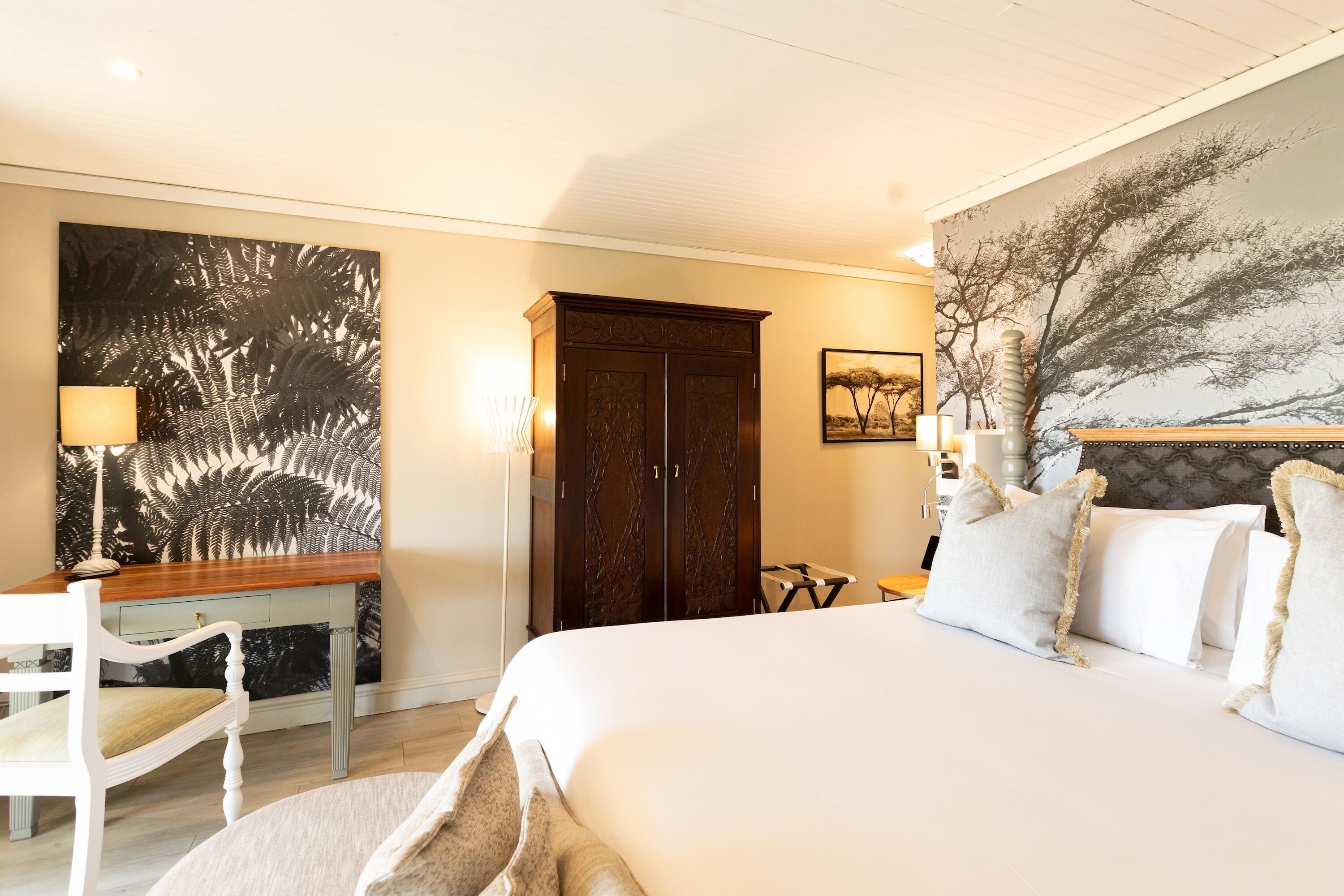 A bedroom with a large bed, a desk, a wardrobe, and a painting on the wall.