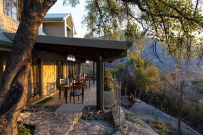 A modern house with a patio area featuring outdoor seating, a stone pathway, and a view of a mountainous landscape. - Rupurara Valley Lodge (Juliasdale)