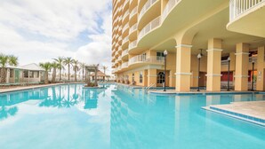 A large indoor swimming pool with a clear blue water surface, surrounded by a multi-story hotel with balconies and palm trees. - Calypso Tower 3  507, 3 Bed,  2 Bath w Gulf Views! (Panama City Beach)