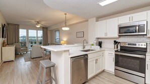 A modern kitchen with white cabinetry, stainless steel appliances, and a central island with a dishwasher. - Calypso Tower 3  507, 3 Bed,  2 Bath w Gulf Views! (Panama City Beach)