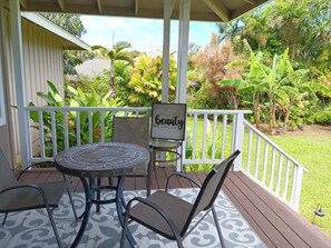 A covered outdoor seating area with a table and chairs, surrounded by a white railing and lush tropical vegetation. - North Shore's Top location~3 bedroom house w/ loft, waterfall views (Princeville)