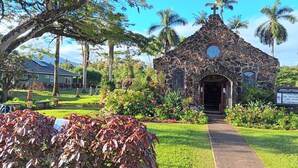 Una iglesia de piedra con una cruz en la parte superior, rodeada de abundante vegetación y palmeras.