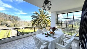 Un balcon avec une table dressée pour le petit-déjeuner, des chaises blanches et une vue sur un palmier et des collines.