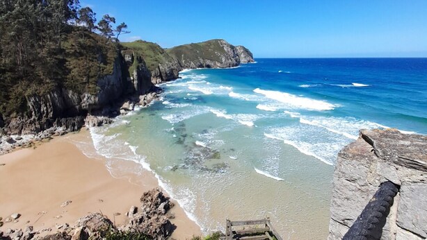 Une plage côtière aux eaux bleues et limpides, bordée de falaises rocheuses et d’un rivage sablonneux.