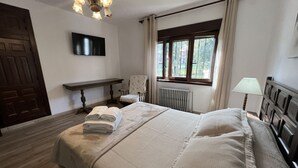 Une chambre bien rangée, avec un lit, un banc, une chaise, un radiateur et une fenêtre avec des rideaux.
