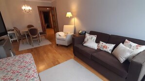 Una sala de estar con un sofá, un televisor, una mesa de comedor con sillas y una lámpara.