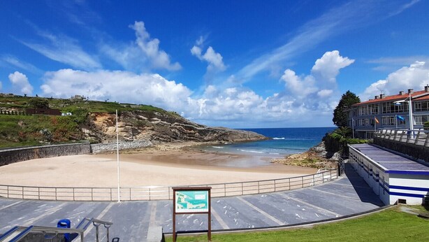 Una playa con una zona de mirador circular, un cartel y un edificio de techo rojo.