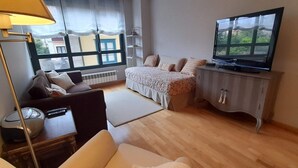 Un dormitorio con cama, televisor, lámpara y ventana con cortinas.