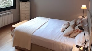 Un dormitorio con una cama grande, una mesita de noche con lámpara, un aparador y una ventana con cortinas.
