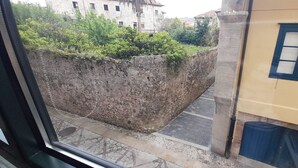 Vista a través de una ventana que muestra un edificio con pared de piedra y una ventana con marco azul.