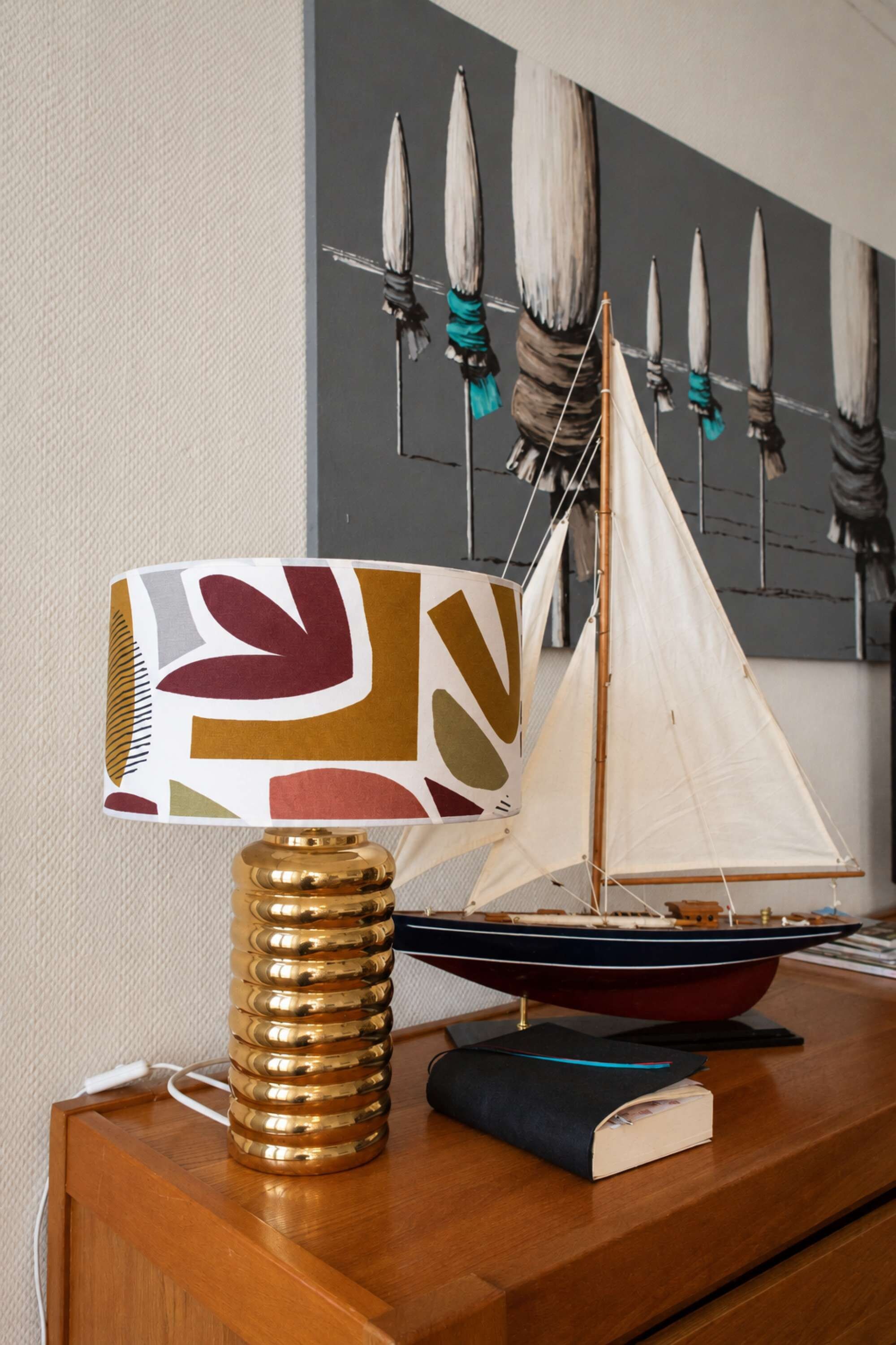 En modellsegelbåt på en träyta, tillsammans med en dekorativ lampa och en bok.