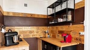 A compact kitchen with a wooden backsplash, a coffee maker, a red kettle, and a black countertop.