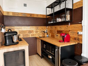 A compact kitchen with a wooden backsplash, a coffee maker, a red kettle, and a black countertop.