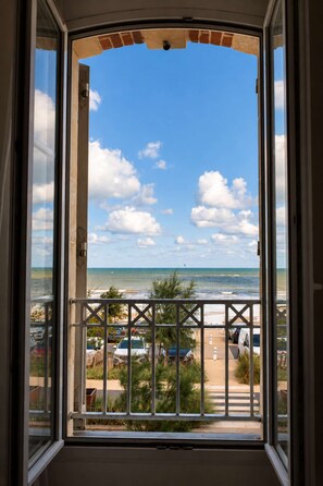 A view through a window with a metal railing, overlooking a beach with parked cars and a clear sky. - Bel Horizon, charming apartment with balcony and sea view (Luc-sur-Mer)