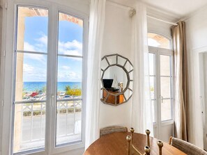 A room with a large window overlooking a beach, a round wooden table, and a decorative mirror on the wall.
