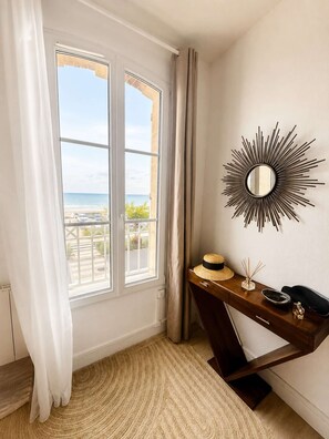 A room with a large window, a sunburst mirror, a wooden desk, and a woven rug.