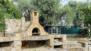 Un horno de piedra al aire libre con chimenea de ladrillo, rodeado de escalones de piedra y follaje.