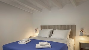 Un dormitorio moderno con una cama grande, dos almohadas blancas y una colcha azul. Hay dos mesitas de noche con lámparas y un cabecero de madera.
