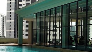 Una piscina con piso de baldosas, rodeada por un edificio con ventanas amplias y un balcón.