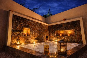 Espacio interior con paredes de piedra, iluminación integrada, una botella y una vela sobre una superficie reflectante.