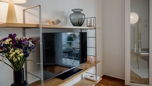 Une chambre moderne avec une télévision posée sur une étagère en bois, un vase et une lampe.
