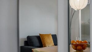Un salon moderne avec un canapé foncé, un coussin de couleur moutarde et une table sur laquelle se trouve un saladier rempli de fruits.