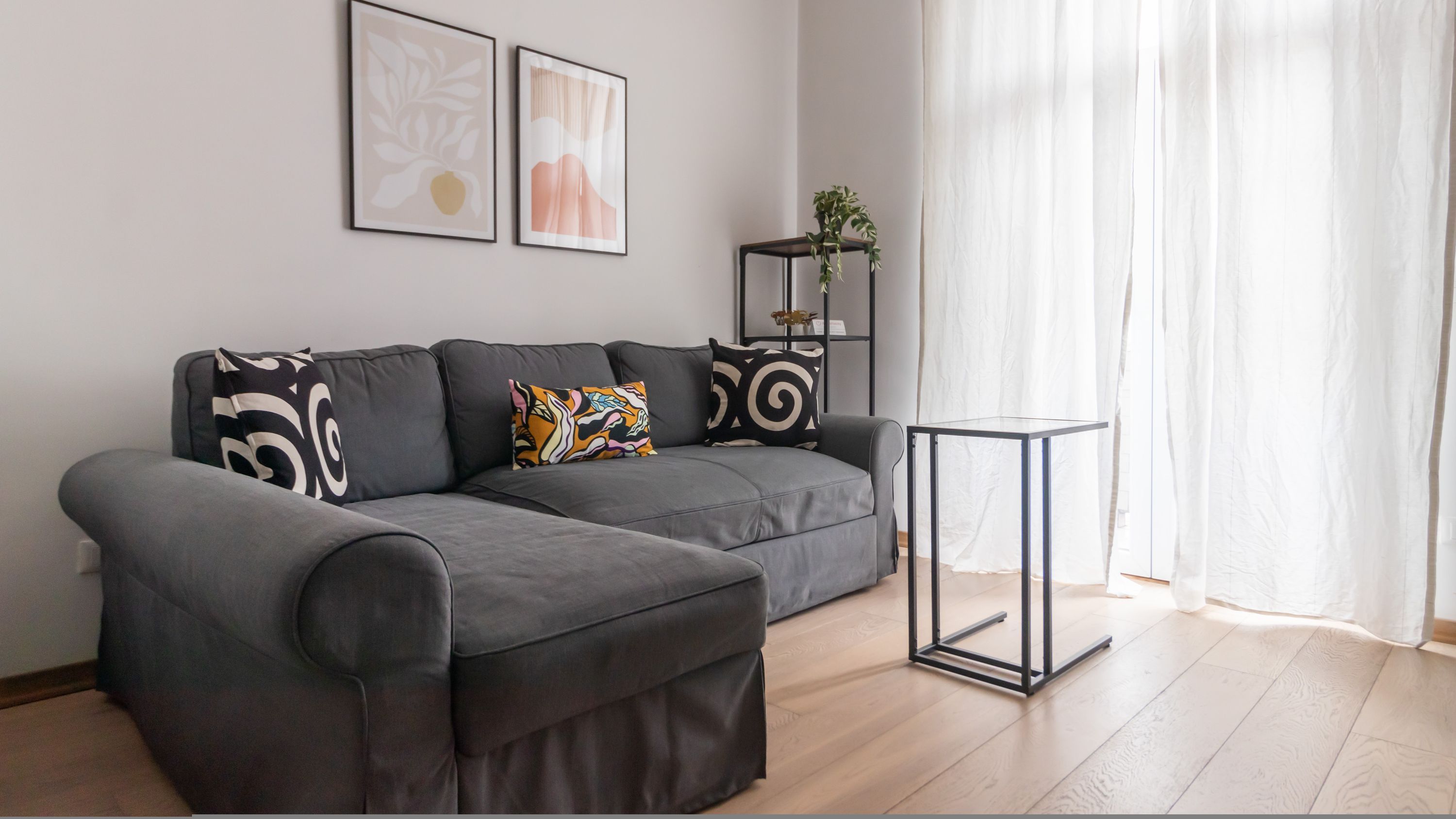 A modern living room with a grey sofa, a small black side table, and two framed artworks on the wall.
