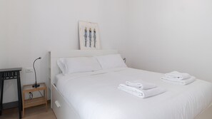 A neatly made bed with white linens and towels, a small wooden nightstand with a lamp, and a framed picture on the wall. - Italianway Comfort - Gallura 9 B (Milan)