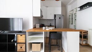 Une cuisine moderne avec des meubles blancs, un îlot central en bois, un téléviseur encastré et une chaise noire.