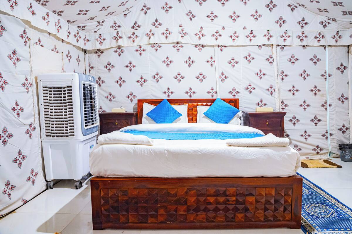 Un dormitorio con cama de madera, ropa de cama blanca, pared con diseño azul y blanco, y aire acondicionado blanco.