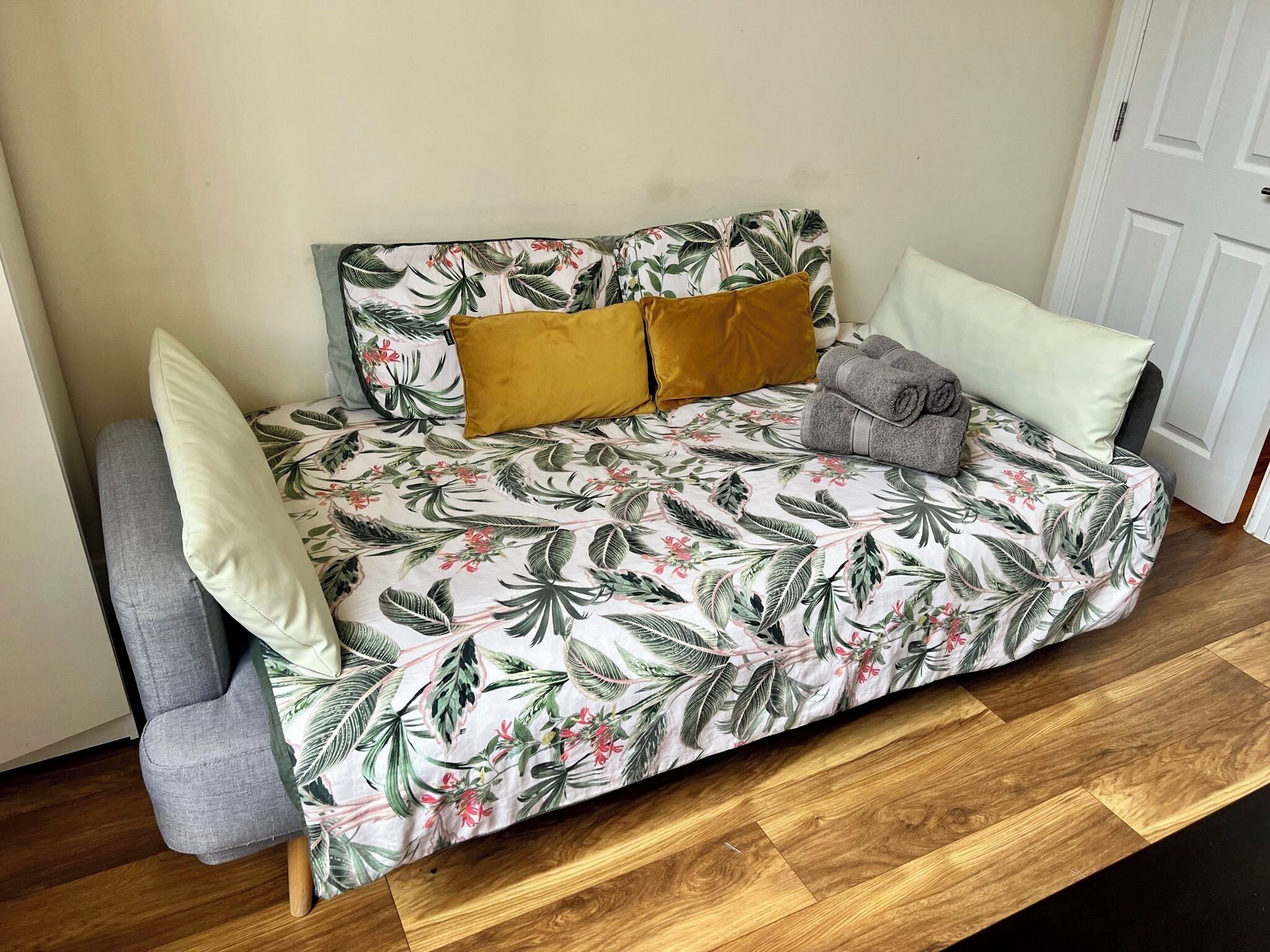 En sovesofa med betræk med blomstermønster, to sennepsgule puder og et sammenrullet gråt håndklæde.