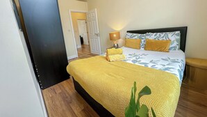 A bedroom with a bed, a bedside table with a lamp, and a door leading to another room. - 2BDR flat in Hammersmith with Wi-Fi & Workspace near Shepherd's Bush & Westfield (London)